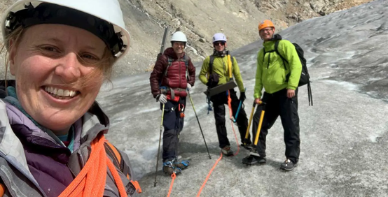 Bethan Davies, left, with colleagues, wearing hard hats and ropes, standing on a glacier