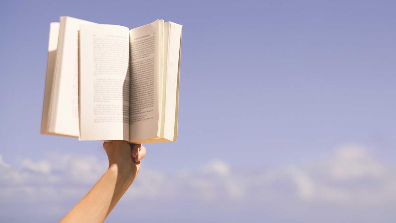 Book in hand against blue sky - English
