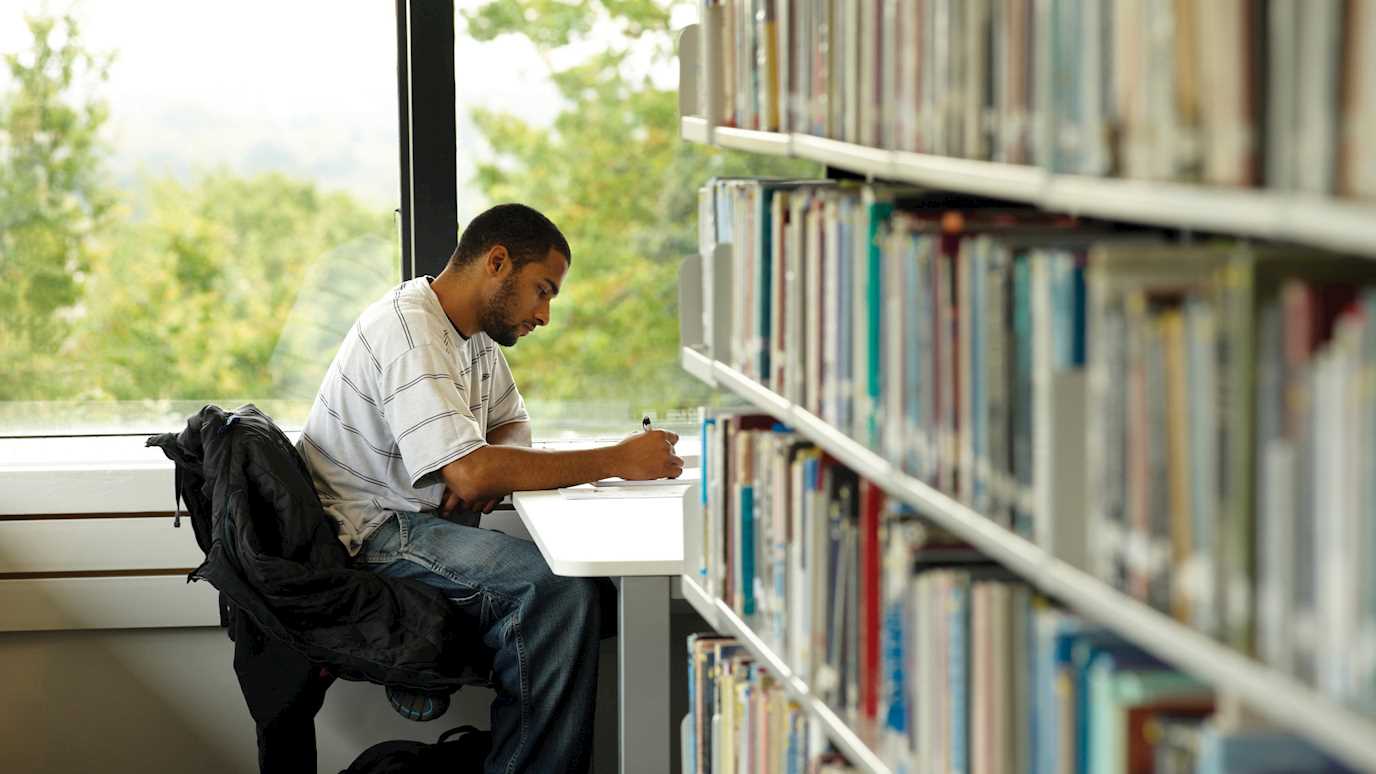 man studying next to a bookshelf - media arts research