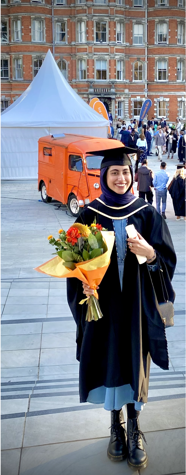 A person in a graduation gown holding flowers
Description automatically generated