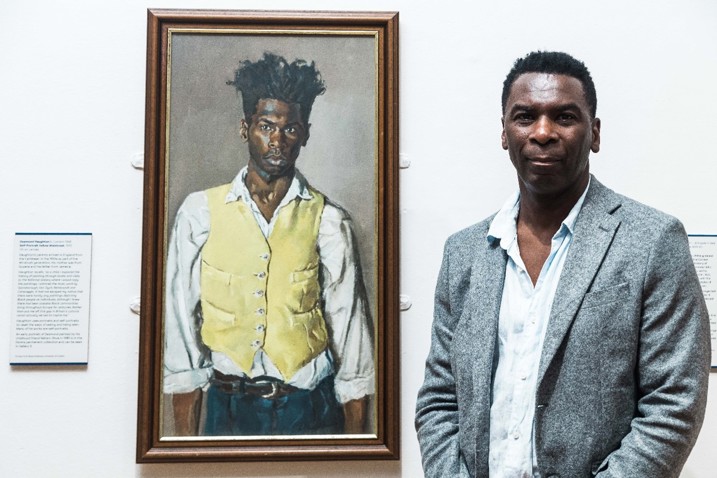 Photograph of the artist Desmond Haughton with his Self Portrait Yellow Waistcoat in the exhibition Seen and Unseen