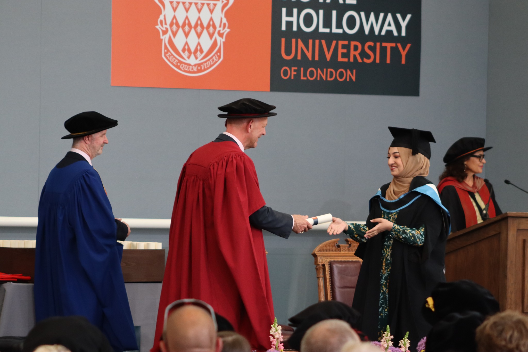 Graduate being handed their scroll by the presiding officer on the ceremony stage